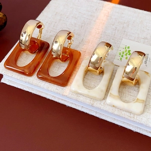 Detail of geometric C-shaped earrings with amber and marble resin charms on linen
