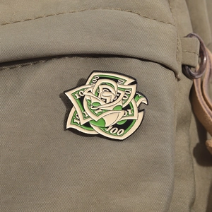 Detail of creative enamel pin shaped like a dollar bill rose on green canvas fabric