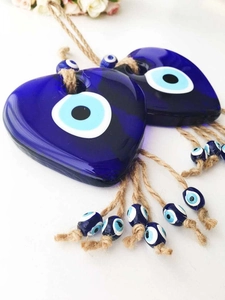 Close-up of heart-shaped blue glass Evil Eye charms with jute rope and floral background