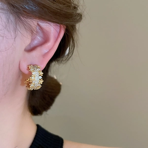 Close-up of golden C-shaped earring with textured finish worn by a model