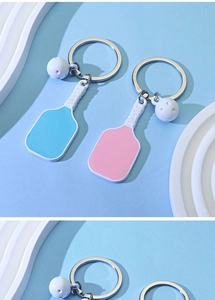 Close-up of pink and blue pickleball paddle keychains with mini balls on blue background