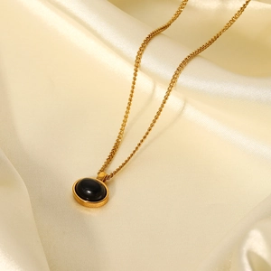 Macro shot of 18K gold plated oval black stone pendant on silk fabric texture
