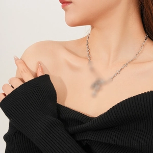 Detail shot of a silver safety pin and cross necklace worn by a model on neck