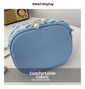 Close-up of light blue denim bucket bag featuring pearl closure and fringe details