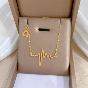 Macro shot of gold heartbeat pendant and heart charm on a chain in a jewelry box