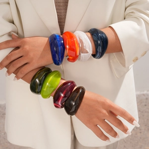 Close-up of a stack of chunky acrylic bangles in various colors on a model wrist