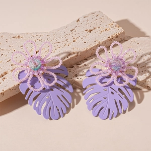 Detailed view of handmade beaded floral and tropical leaf earrings on stone