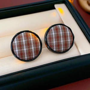 Macro shot of coffee brown checkered fabric button earrings on a white velvet cushion