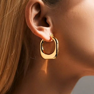 Close-up of gold chunky square hoop earrings with polished finish on model's ear
