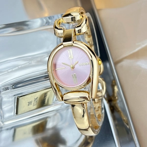 Detailed close-up of a vintage gold bracelet watch with a pink textured dial on glass