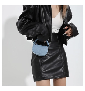 Detail of light blue denim mini handbag featuring metal hardware on a leather outfit