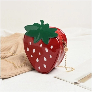 Close-up of strawberry-shaped red patent leather crossbody bag with golden chain strap