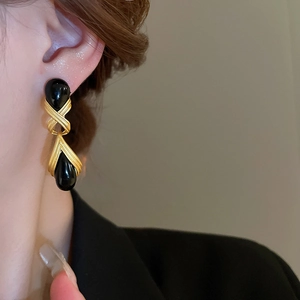 Detail of vintage gold metal earrings with black resin water drop charms worn by model