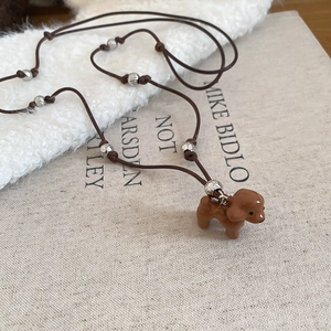 Détail d'un mignon pendentif chien en émail marron sur un collier cordon avec perles