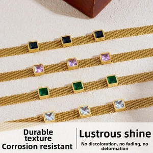 Detail view of woven gold chain bracelets with colorful square zircon stones on stone background