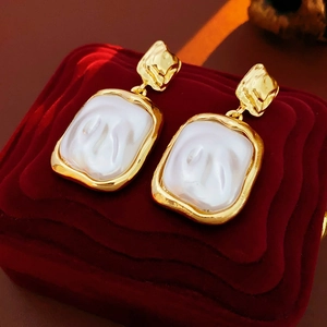 Macro shot of gold square baroque pearl earrings on a luxurious red velvet background