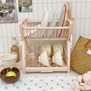 Pink two-tier plastic dish drying rack with organized kitchenware on a kitchen counter