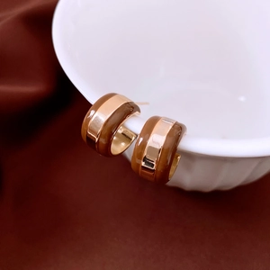Detailed view of striped C-shaped earrings in coffee brown and gold on white ceramic