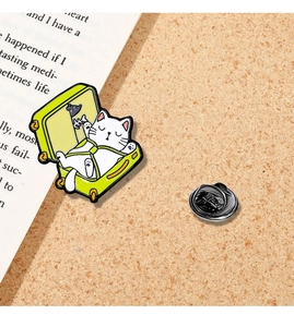 Close-up of a white cat enamel pin in a green suitcase on a corkboard with a book