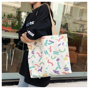 Detailed view of cream canvas tote bag with colorful geometric patterns on a model's shoulder