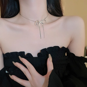 Detail of silver metallic bow pendant snake chain necklace worn on a model's neck