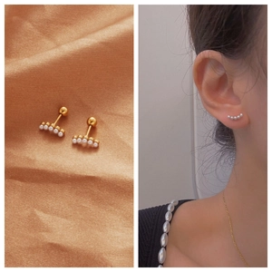 Macro detail of gold pearl cartilage studs featuring five small pearls with screw ball back