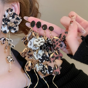 Detail of leopard print fabric flower drop earrings with black gemstone studs and gold chain