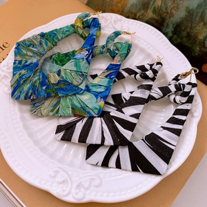Macro shot of large geometric earrings featuring blue abstract and zebra fabric wraps