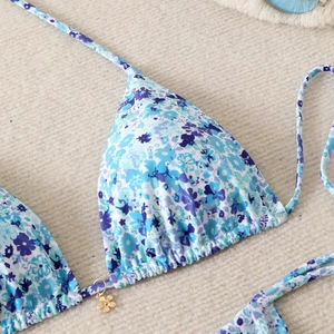 Detailed macro view of blue floral bikini top with a golden flower pendant and halter ties