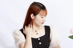 Detailed view of red evil eye necklace and earring set on model with gold finish