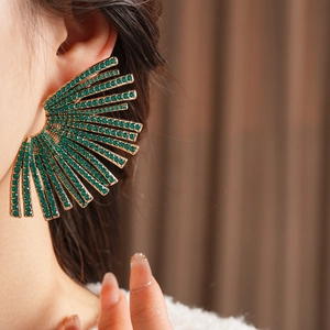 Detail of a fan-shaped earring with emerald green rhinestones worn by a model