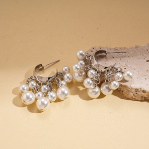 Detail of silver C-shape tassel earrings with layered faux pearls on a textured rock