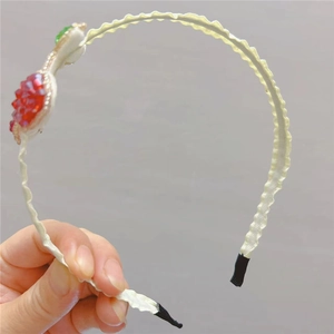 Detail of a white wavy headband with handcrafted red strawberry and green leaf beads