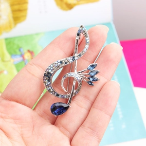 Macro detail of G-clef brooch featuring colorful rhinestones and blue teardrop gem