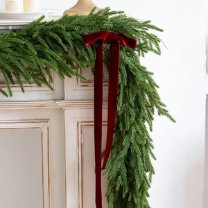 Norfolk pine Christmas swag with long red velvet ribbon hanging on a white fireplace