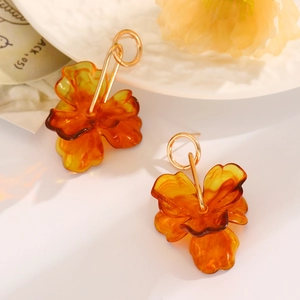 Macro detail of amber resin flower earrings with gold hooks on a white ceramic plate
