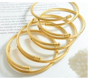 Macro view of gold twisted cable bracelets with threaded cylinder ends on white table
