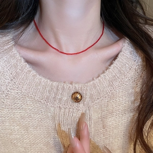 Detail of minimalist red crystal beaded necklace worn over a white knitted sweater