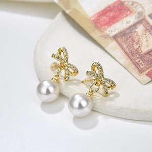 Elegant gold bow earrings with white pearls and sparkling crystals on ceramic tray