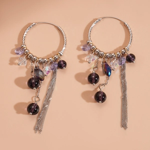 Silver hoop earrings featuring purple crystal beads and metallic chain tassels on peach background
