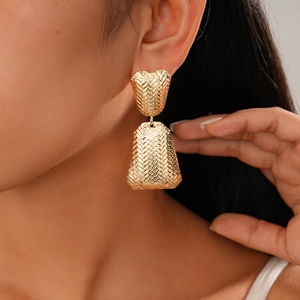 Detailed close-up of a model wearing gold metal earrings with a woven textured design