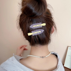 Detail of purple and yellow matte triangle hair clips paired with a classic pearl necklace