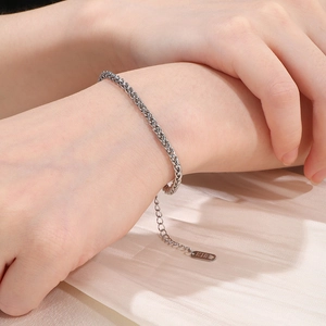 Close-up of silver wheat chain bracelet with K18 engraved tag on soft fabric background
