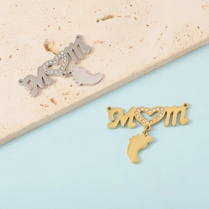 Polished silver and gold MOM heart charms with baby feet pendants on stone background