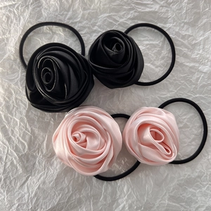 Detail of four satin rose hair ties in black and pink on a white textured background