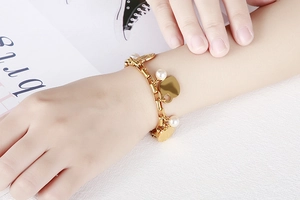 Gros plan d'un bracelet doré avec breloque cœur et perles porté sur le poignet