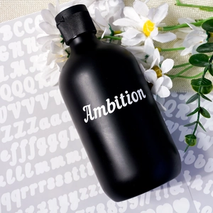 Detail showing white Ambition lettering on a matte black bottle with vinyl alphabet stickers