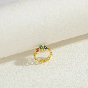 Close-up of gold geometric heart ring featuring colorful red, green, and blue zircon stones