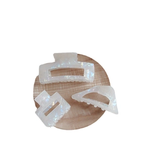 Iridescent white acetate hair claw clip set with three geometric shapes on wood base