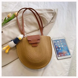 Detail of semi-circle straw tote bag with leather strap and cute duck charm accessory